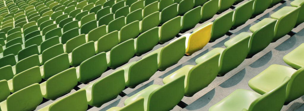 Rows of green chairs in a stadium with one yellow chair.