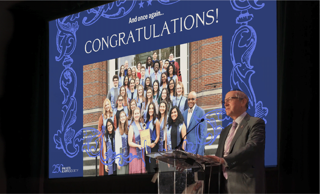 Phi Beta Kappa's president Frederick Lawrence giving a speech in front of a screen with a projected image of Phi Beta Kappa inductees and the word 
